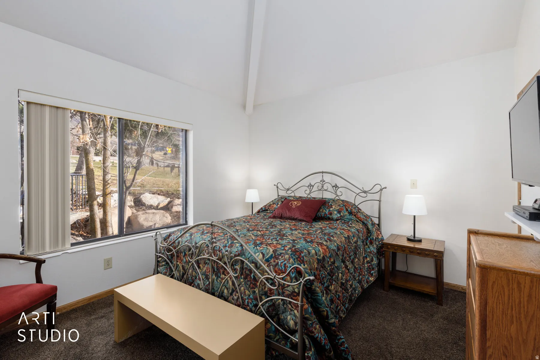 Bedroom with vaulted ceiling, large picture window, dark carpeting, and a built-in wood-finish cabinet