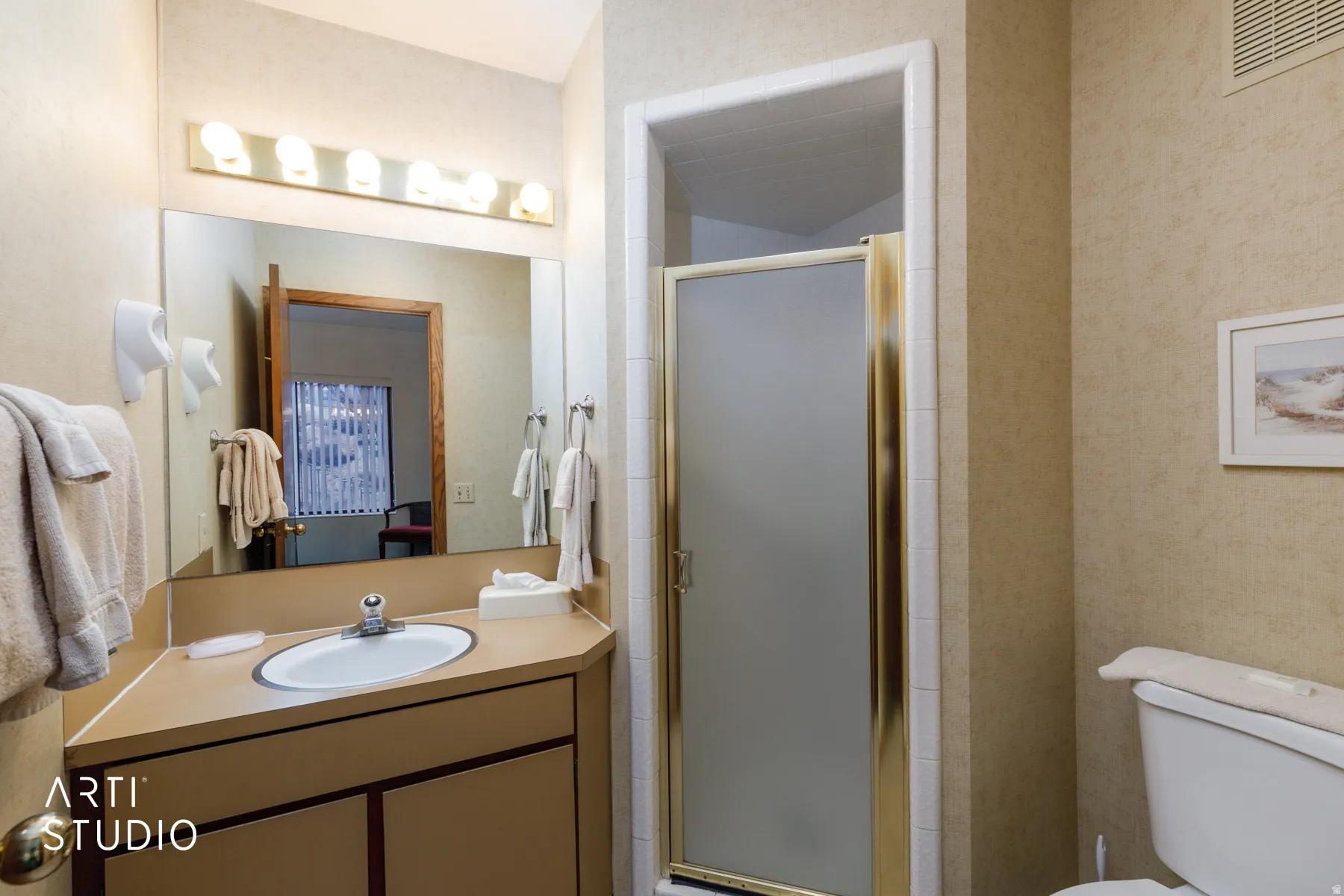 Compact bathroom featuring a corner vanity with an integrated sink, a rectangular mirror, and a shower enclosure with frosted glass and gold-tone framing