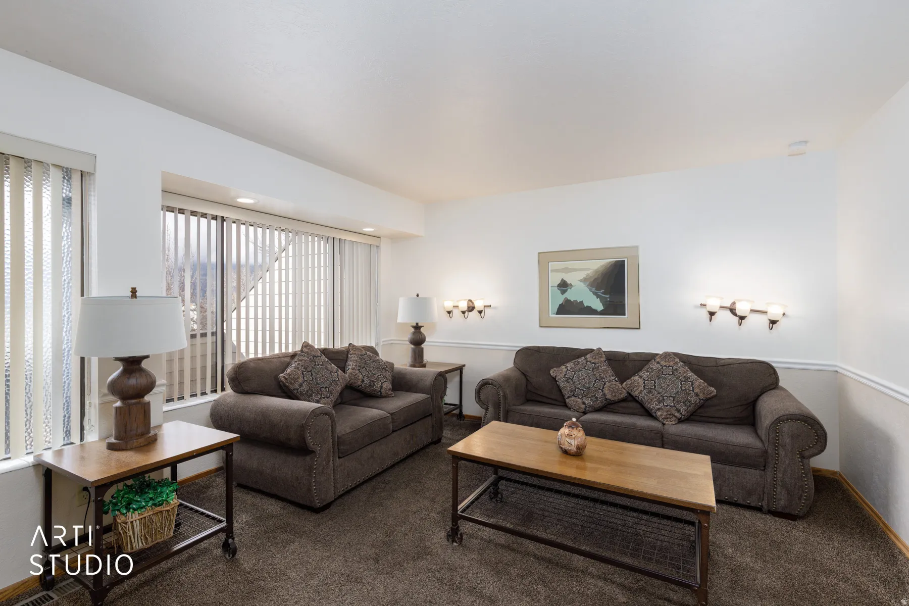 Bright living area featuring white walls, deep brown carpeting, and a large bay window