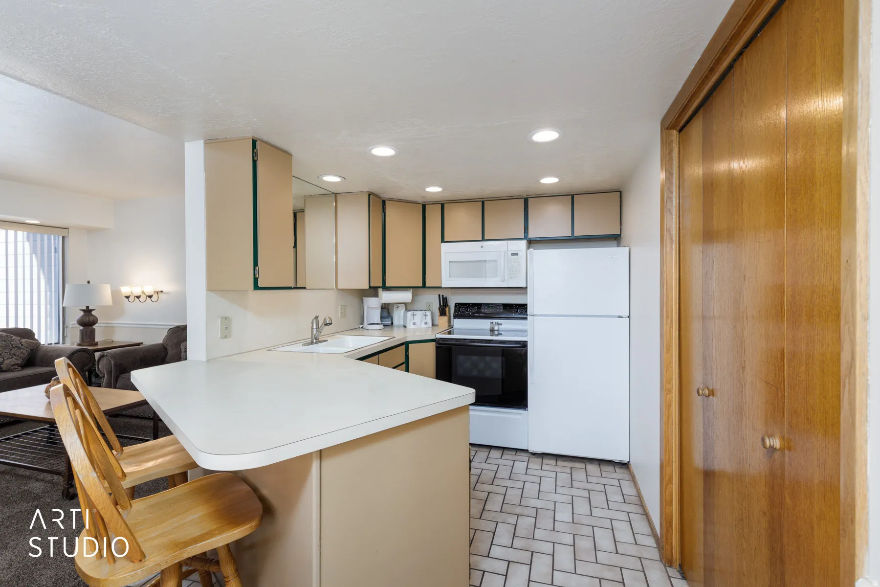 Kitchen featuring cream cabinetry, white appliances, a peninsula with counter seating, recessed lighting, and herringbone tile flooring