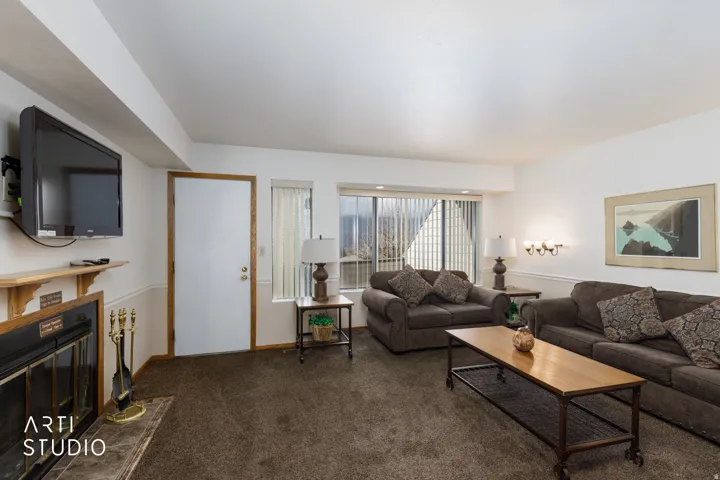 Living area featuring a fireplace with a wood mantle and dark-toned carpet flooring