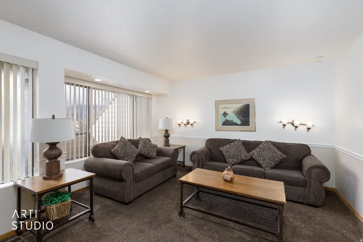 Bright living area featuring white walls, deep brown carpeting, and a large bay window