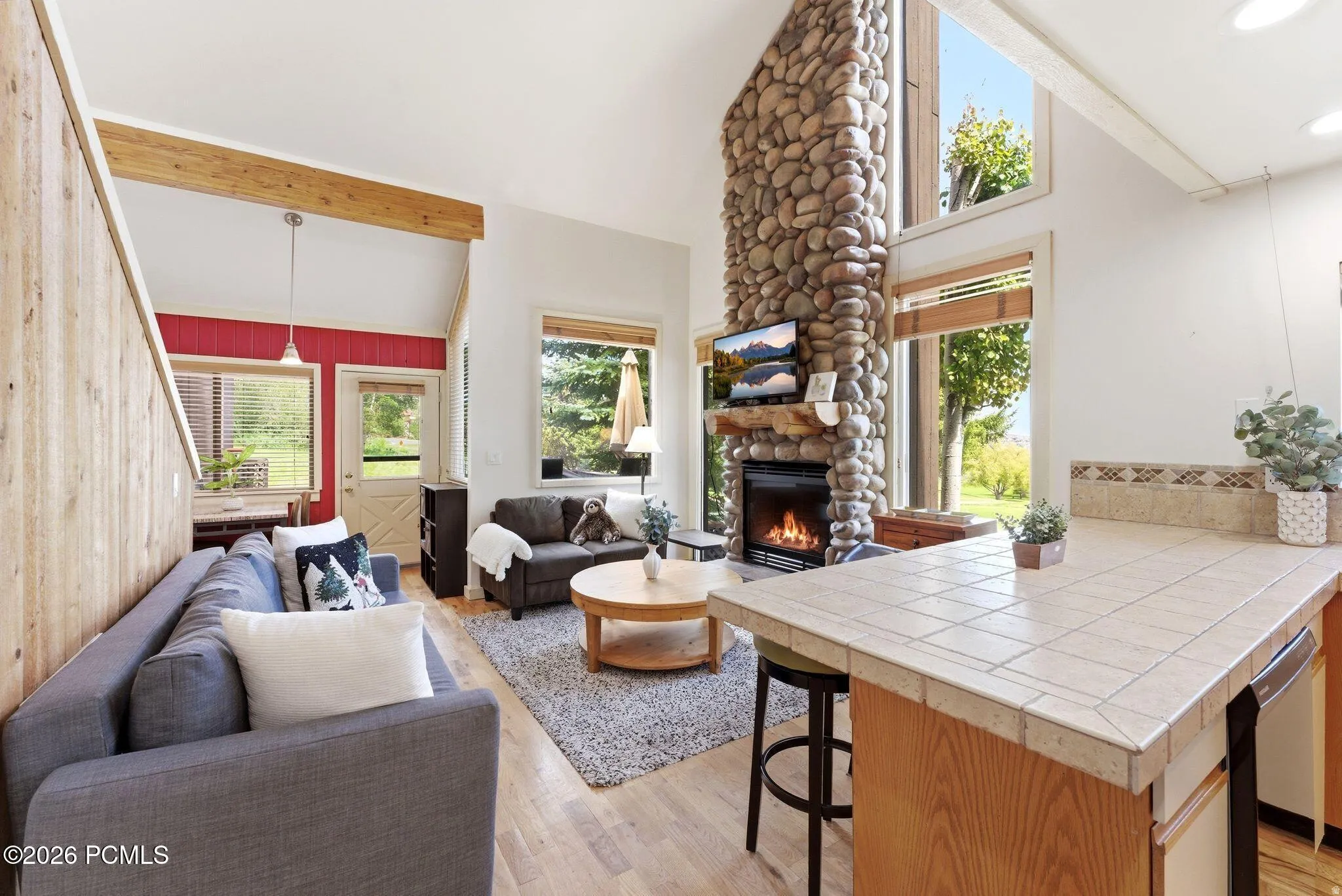 Living area featuring a floor-to-ceiling stone fireplace, vaulted ceilings, and light wood-finish flooring