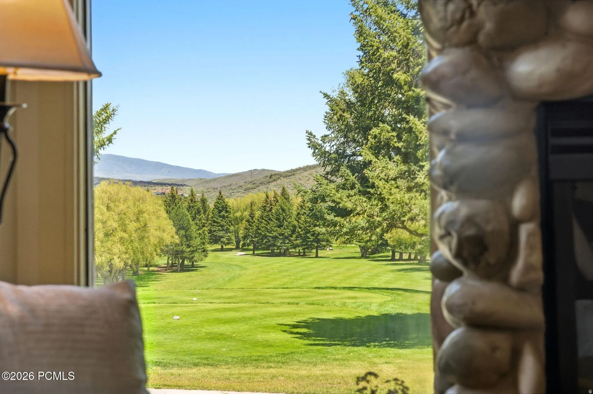 Expansive golf course frontage with mature evergreen trees and distant mountain ranges