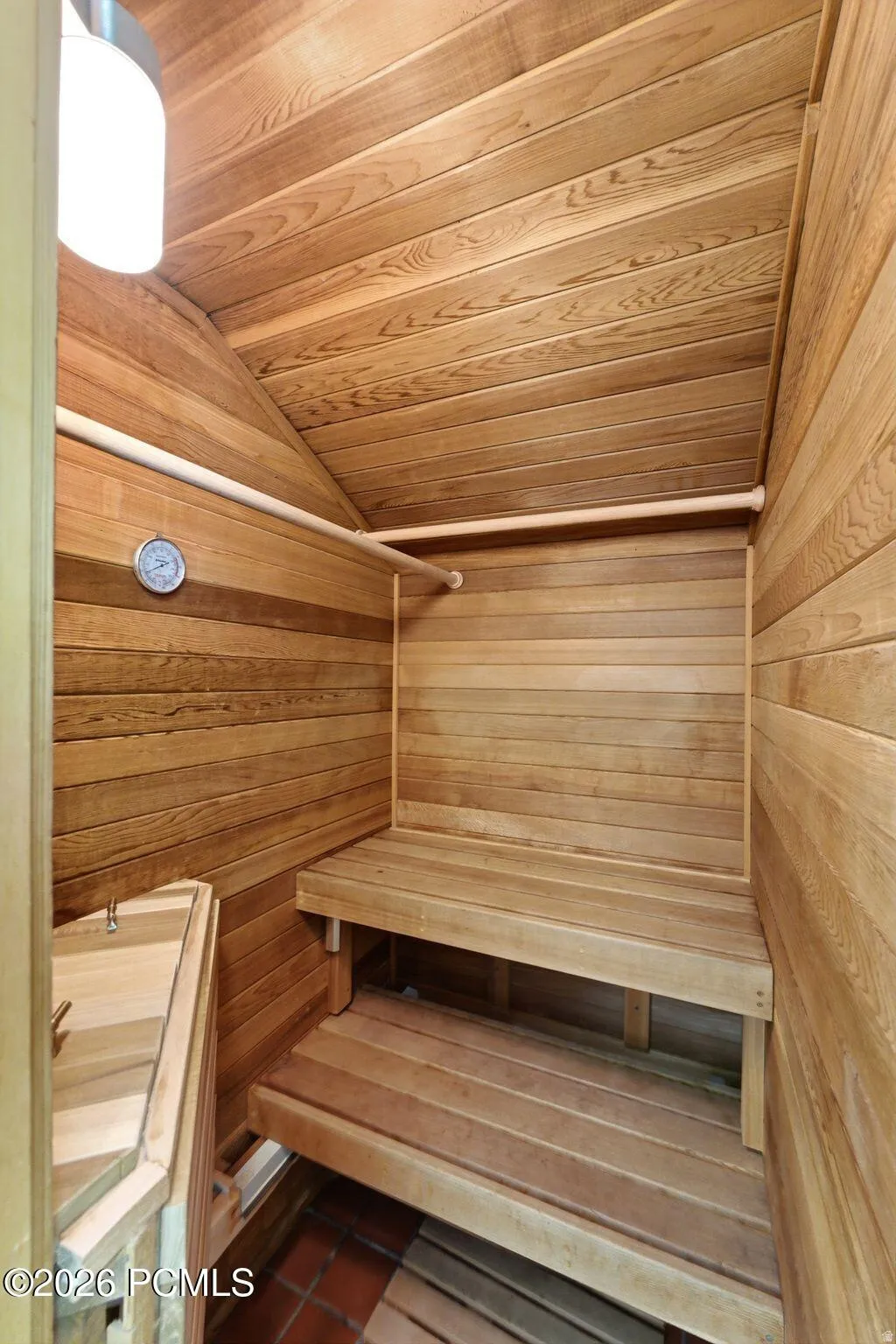 Wood-paneled sauna featuring tiered wooden benches, sloped ceiling, and a wall-mounted thermometer