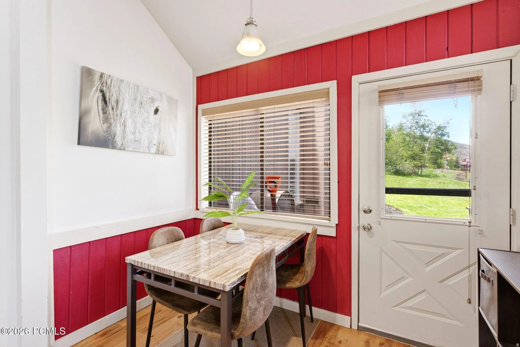 Dining area featuring red vertical paneling, light wood-finish flooring, a window with blinds, and a white exterior door with a window pane