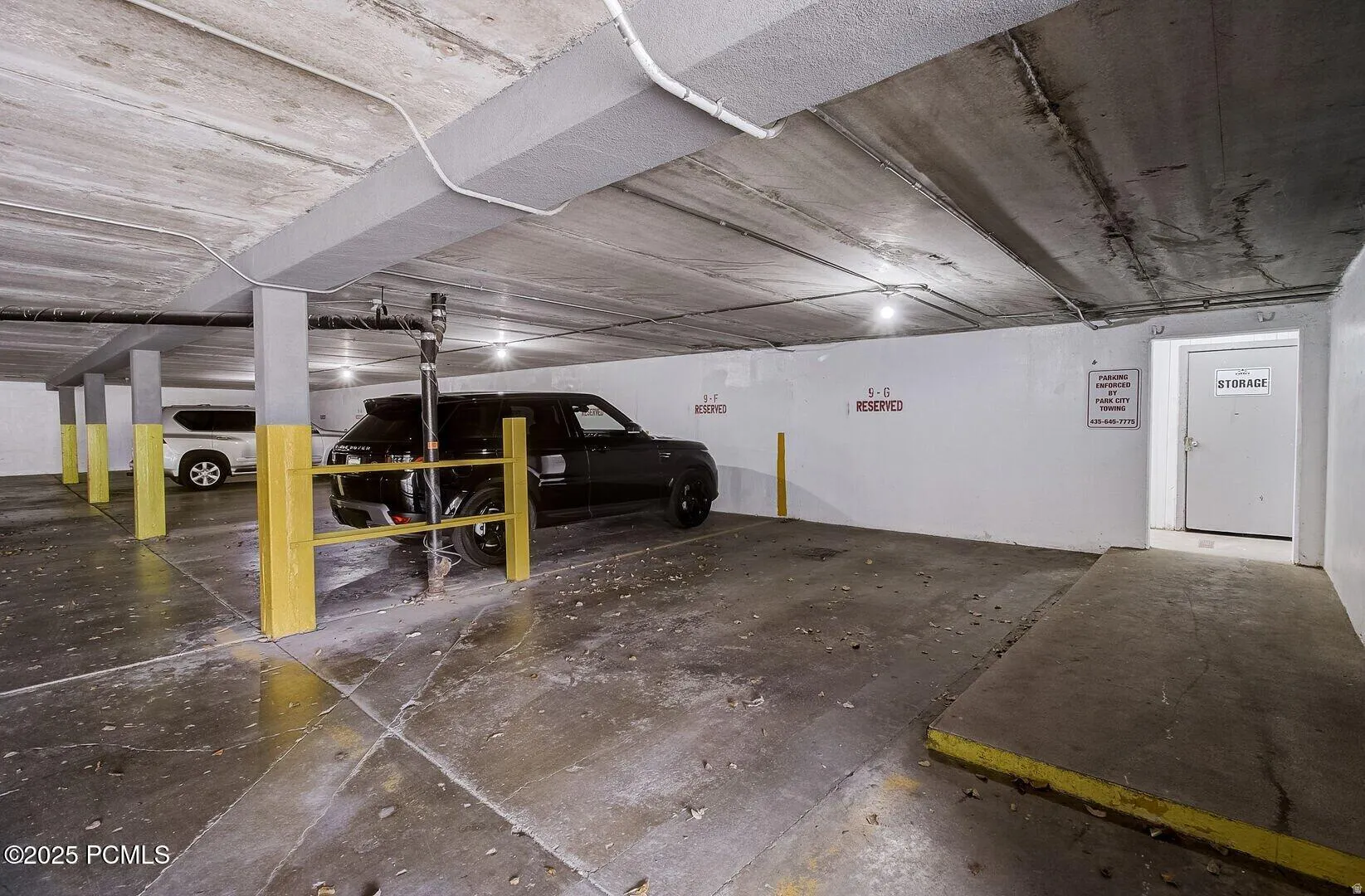 Underground parking garage featuring concrete flooring, exposed concrete ceiling, support columns with protective yellow guards, and a dedicated storage room entrance