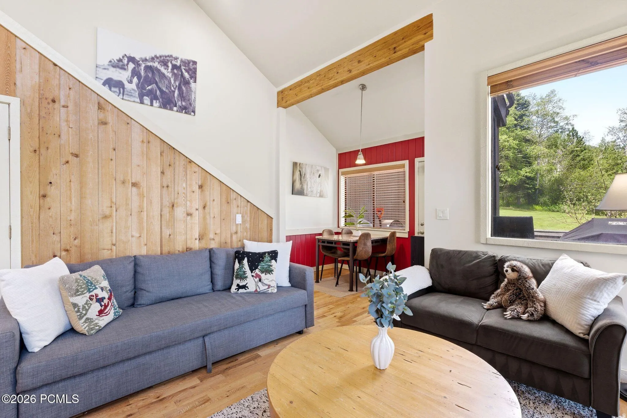 Open-concept living space with vaulted ceilings, natural wood accent wall, and wood-finish flooring