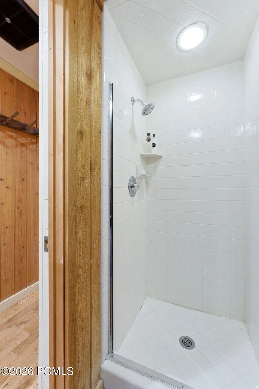 Shower enclosure with white subway tile walls, chrome fixtures, and an overhead light