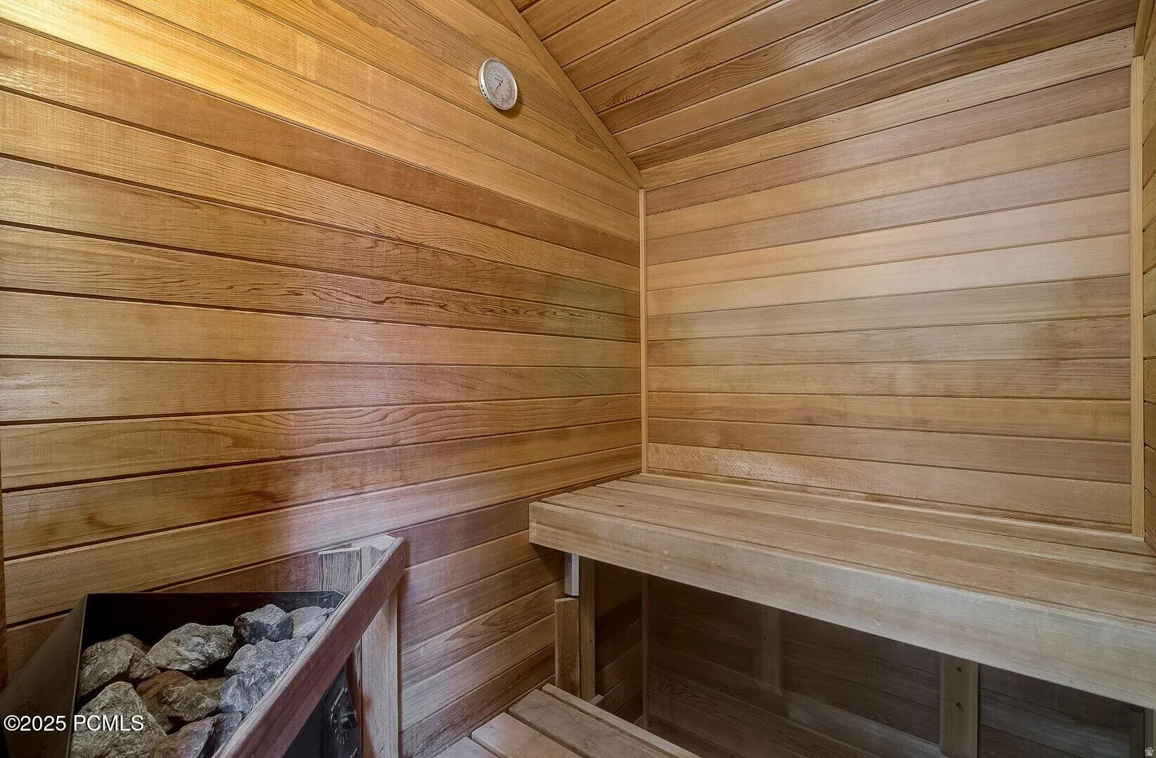 Sauna featuring wood-plank walls and ceiling, built-in wooden bench, and a rock-filled heater unit