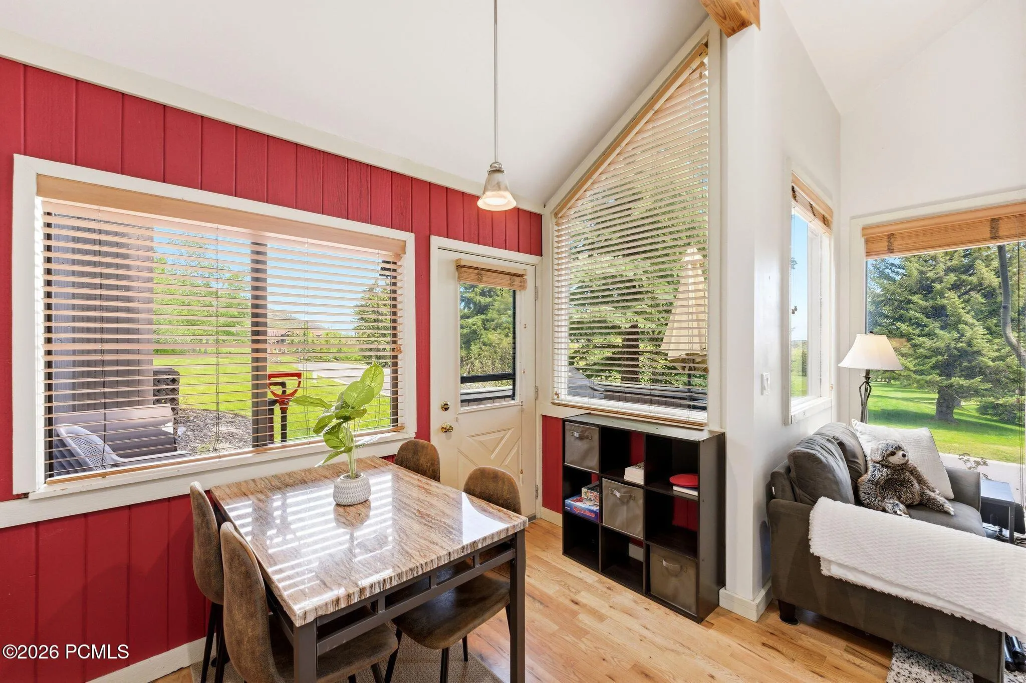 Dining area featuring a wood-finish table, a decorative pendant light, and a prominent window with horizontal blinds
