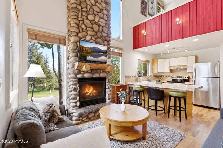 Vaulted ceiling living space featuring a floor-to-ceiling stone fireplace, natural wood mantel, and large windows