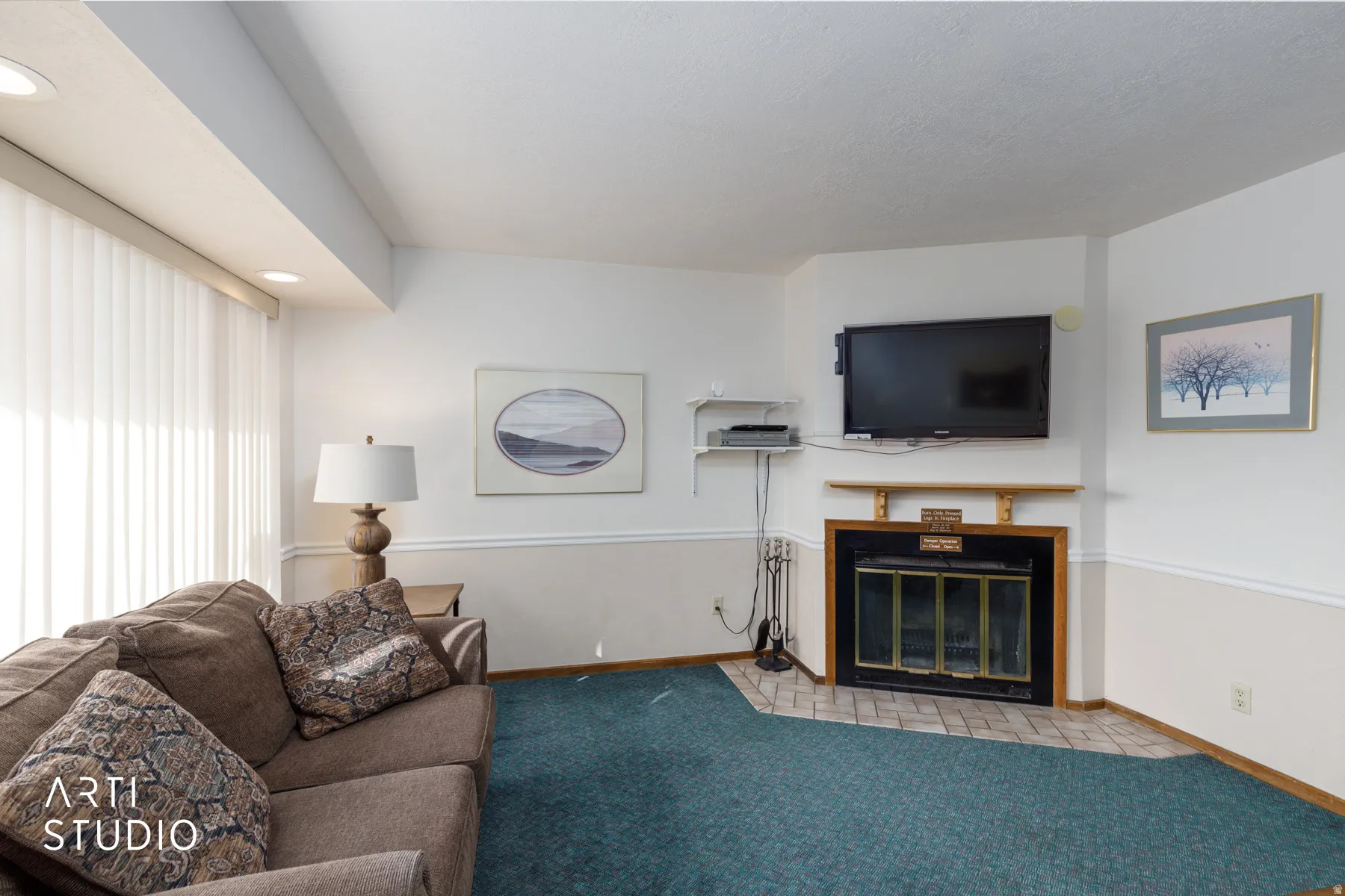 Living area featuring a corner fireplace with a black framed glass door, a wood mantel, and a tiled hearth
