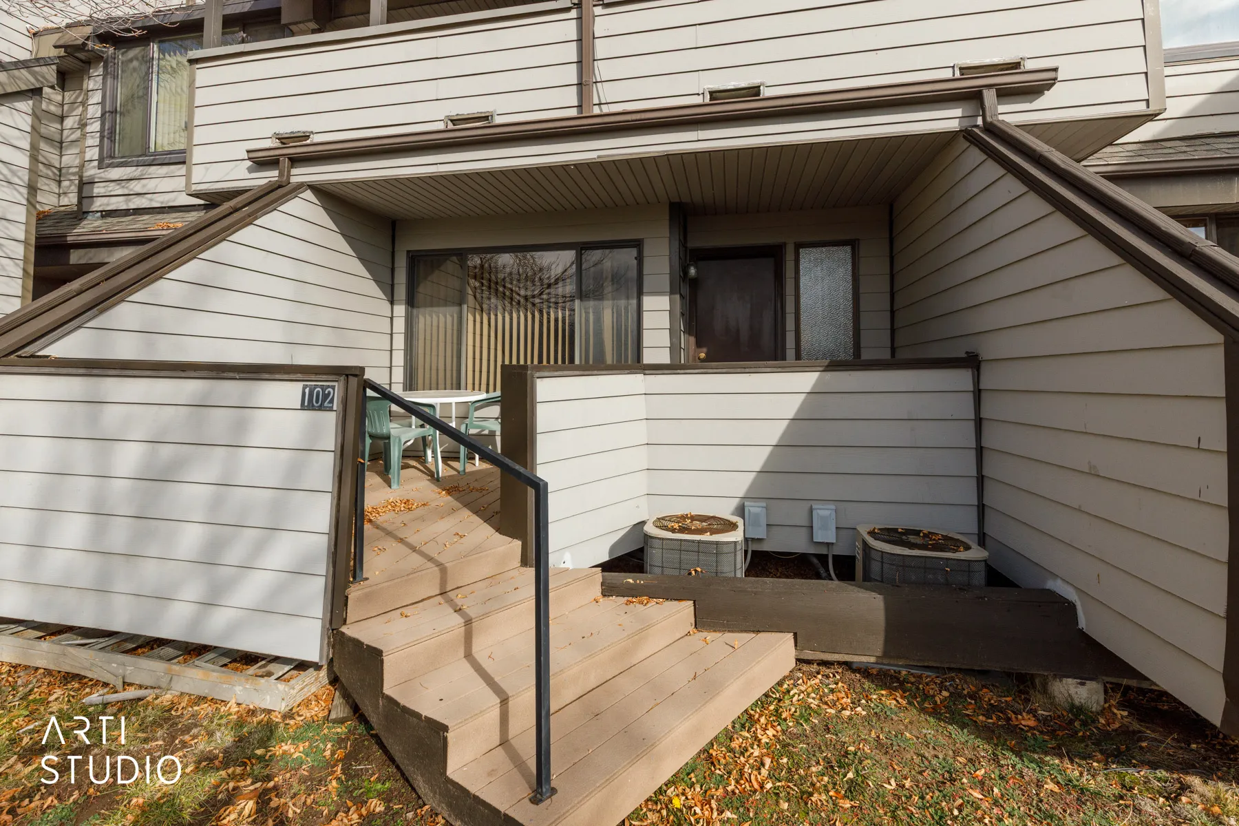Exterior entrance featuring wooden steps with a black metal handrail, leading to a covered patio space