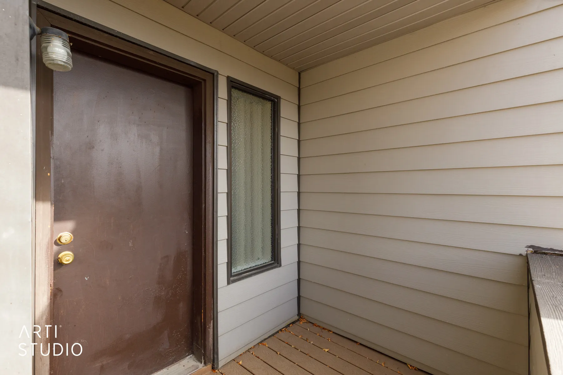 Entryway featuring a brown door with brass hardware, an exterior light fixture, horizontal siding, and a vertical window with obscured glass