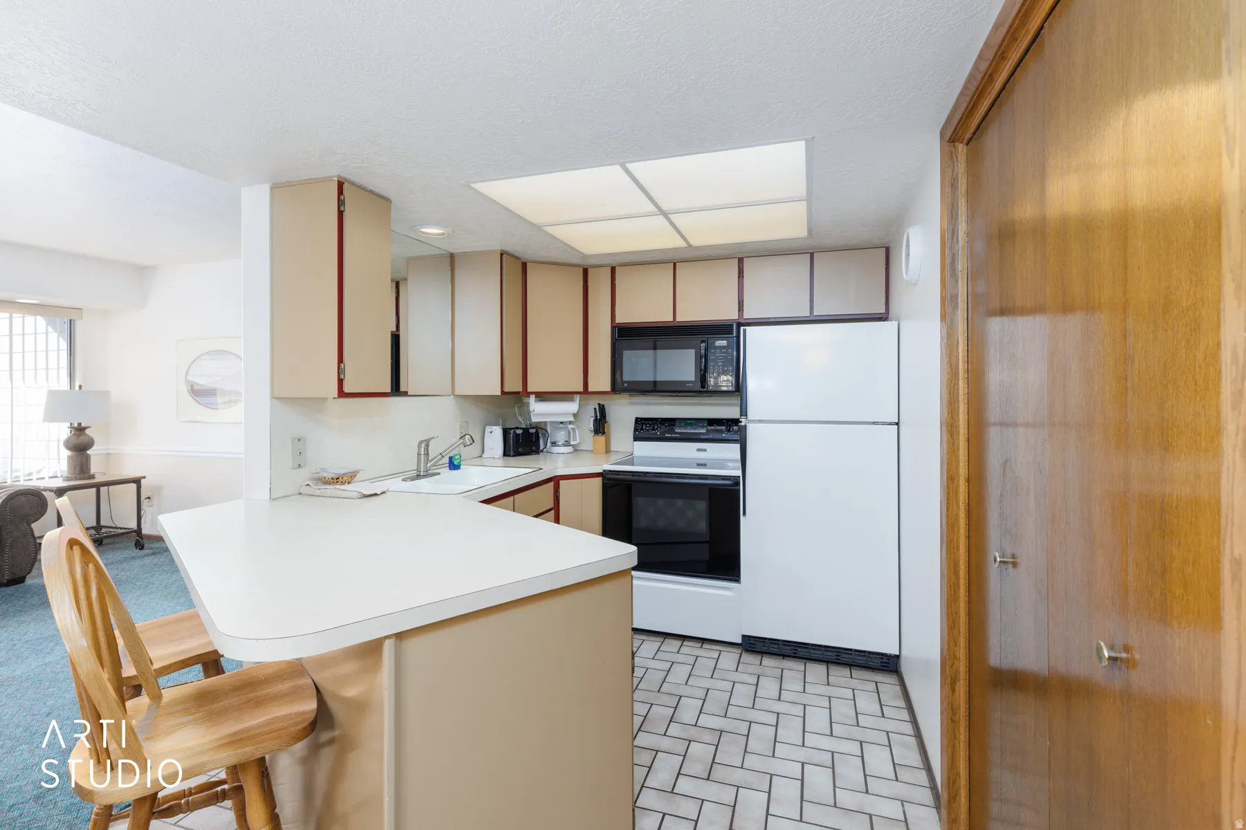 Kitchen featuring a breakfast bar, white countertops, tan cabinetry with red trim, white appliances including a refrigerator and oven, and a tiled floor