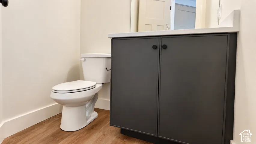 Bathroom featuring a dark grey vanity cabinet with matte black hardware, light-toned countertop, white vitreous china toilet, and wood-finish flooring