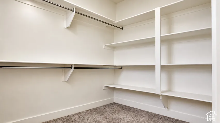 Walk-in closet featuring white wooden shelving, multiple tiers of built-in storage, and wall-mounted metal hanging rods