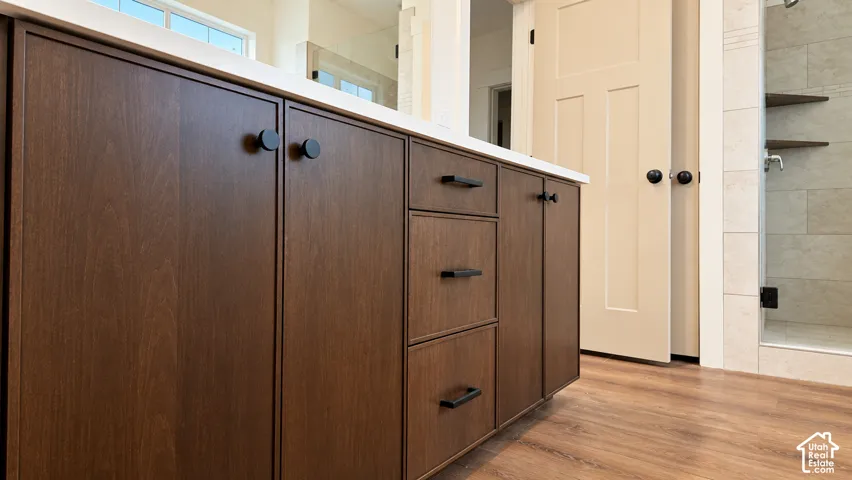Bathroom vanity with dark wood-finish cabinetry, white countertop, matte black hardware, and wood-finish flooring, featuring a tiled shower enclosure with built-in corner shelving