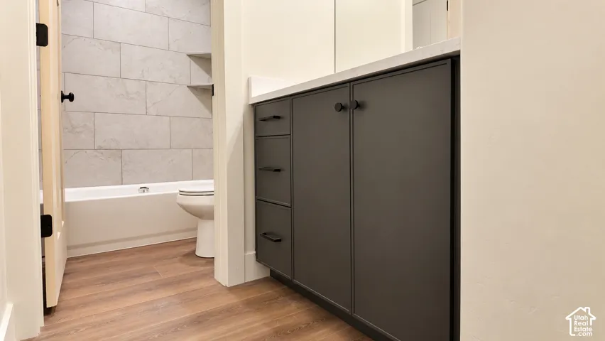 Bathroom featuring a custom dark-finish vanity with matte black hardware, light-toned countertop, wood-finish flooring, and a bathtub surround with rectangular stone-patterned tile