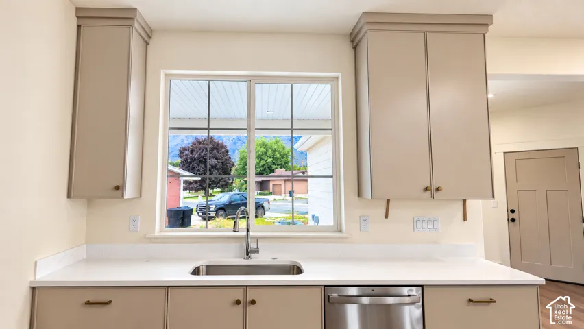 Kitchen featuring neutral-toned cabinetry, solid surface countertops, a stainless steel under-mount sink with a gooseneck faucet, stainless steel dishwasher, and a multi-pane window