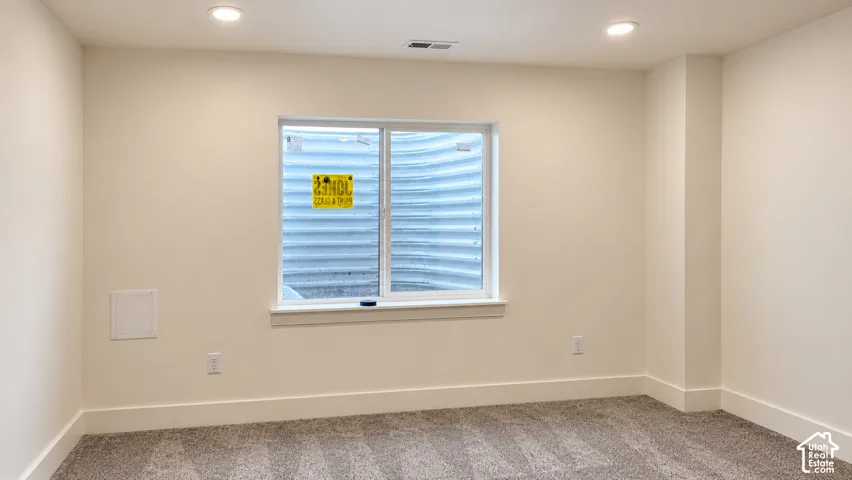 Neutral-toned interior space featuring recessed ceiling lighting, wall-to-wall carpeting, and a sliding window with an integrated egress well