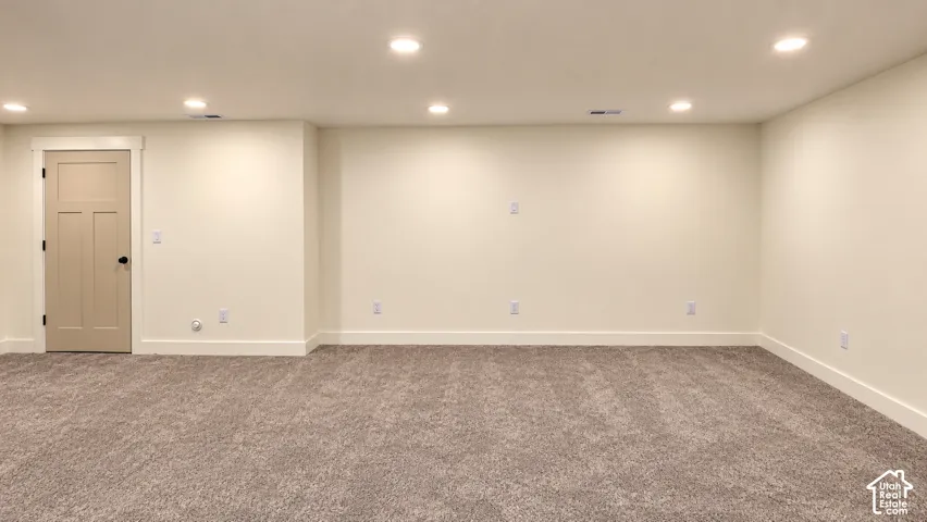 Neutral-toned interior space featuring wall-to-wall carpeting, recessed ceiling lighting, and a single-panel interior door with matte black hardware
