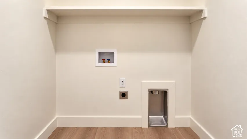Dedicated laundry space featuring wood-finish flooring, a full-width built-in shelf, recessed utility box with hot and cold water hookups, and a recessed dryer vent