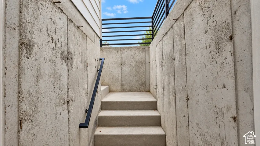 Concrete staircase featuring poured-in-place retaining walls, matte black metal railing, and horizontal steel bar perimeter fencing