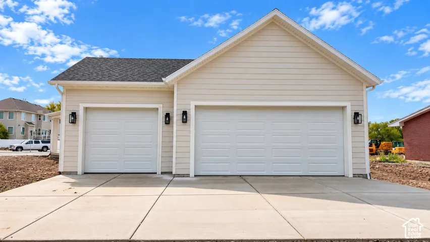 Three-car garage exterior with horizontal siding, a pitched roof, concrete driveway, and wall-mounted exterior lanterns