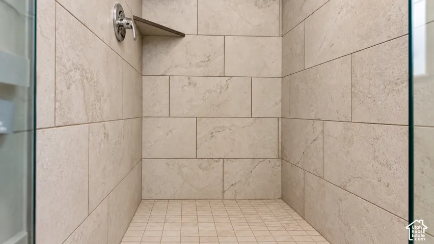 Shower enclosure featuring large-format neutral-tone tile walls, integrated corner shelving, mosaic tile flooring, and a polished metal shower fixture