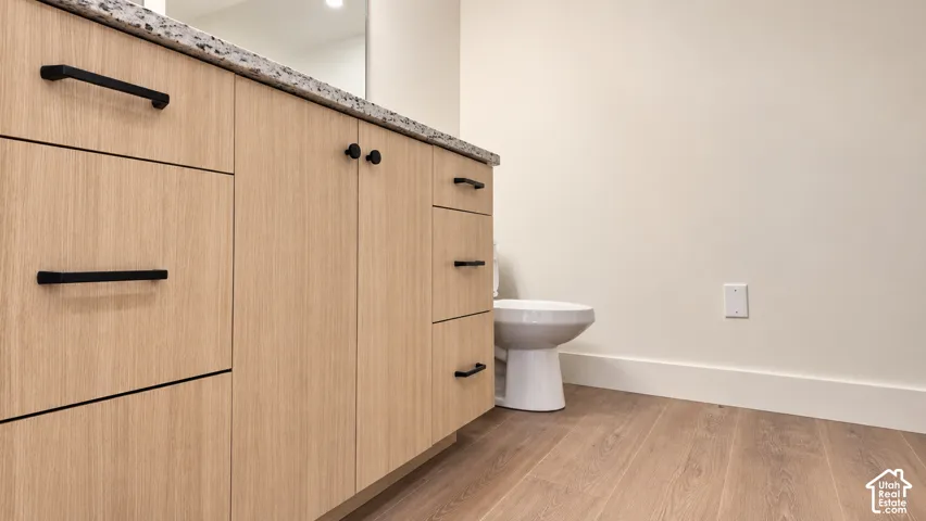 Vanity featuring light wood-finish cabinetry, stone-style countertop, matte black hardware, and wood-finish flooring