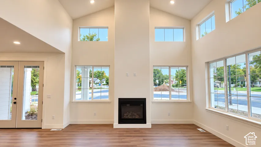 Vaulted ceilings, floor-to-ceiling fireplace with black surround, wood-finish flooring, recessed lighting, and expansive grid-pane windows