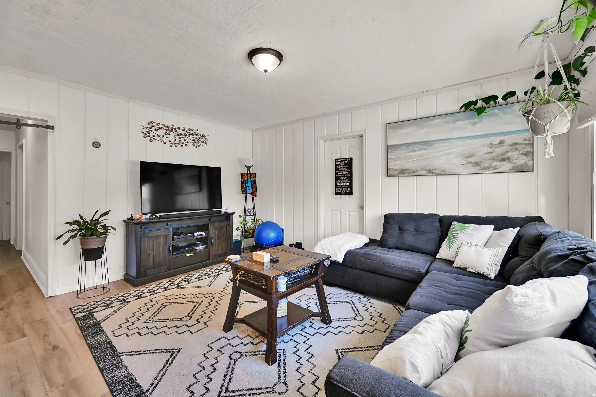 Spacious living area featuring wood-finish flooring, white vertical wall paneling, and an overhead flush-mount light fixture