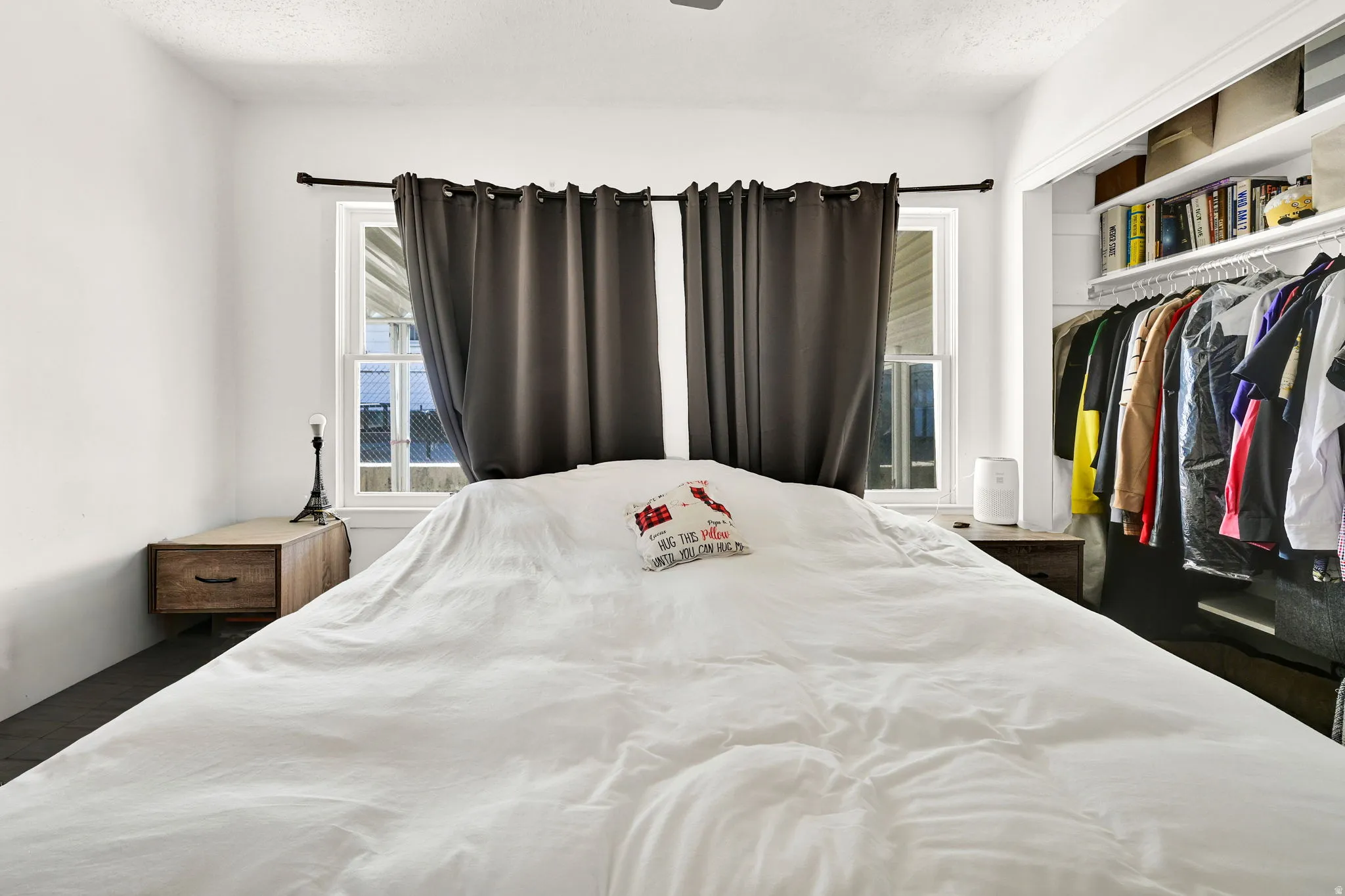 Bedroom featuring two windows with dark curtains, white walls, and dark flooring