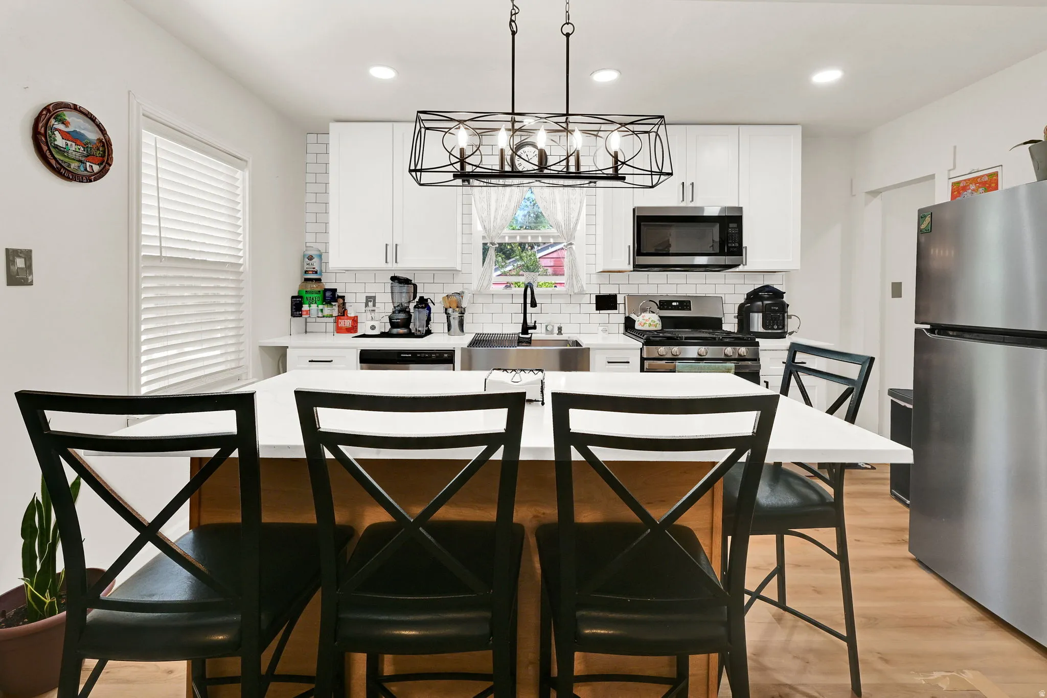 Updated kitchen featuring white shaker cabinetry, stainless steel appliances, subway tile backsplash, and a central island with a light-colored countertop