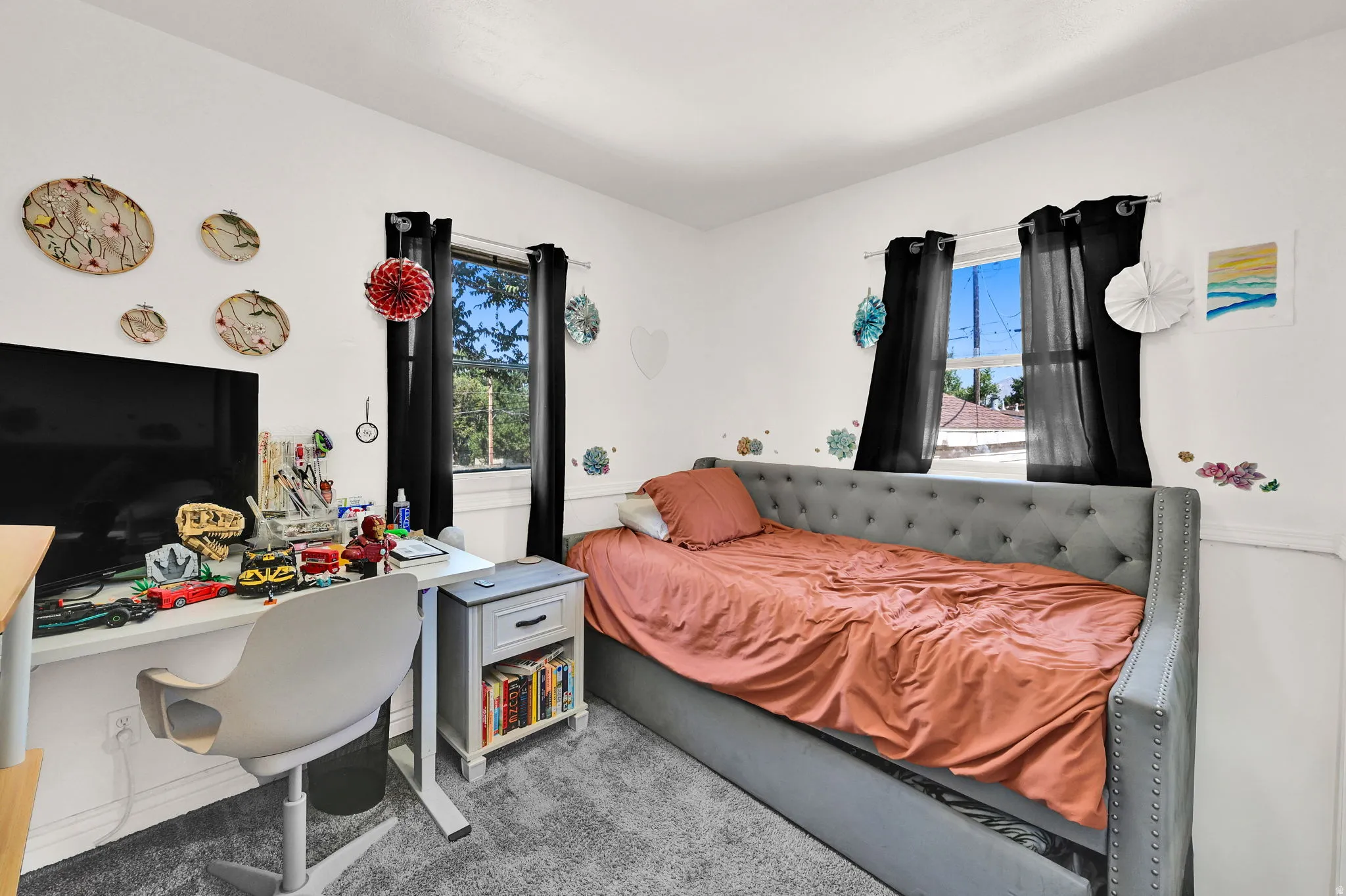 Bedroom featuring two windows with black curtains, white walls, and gray carpet