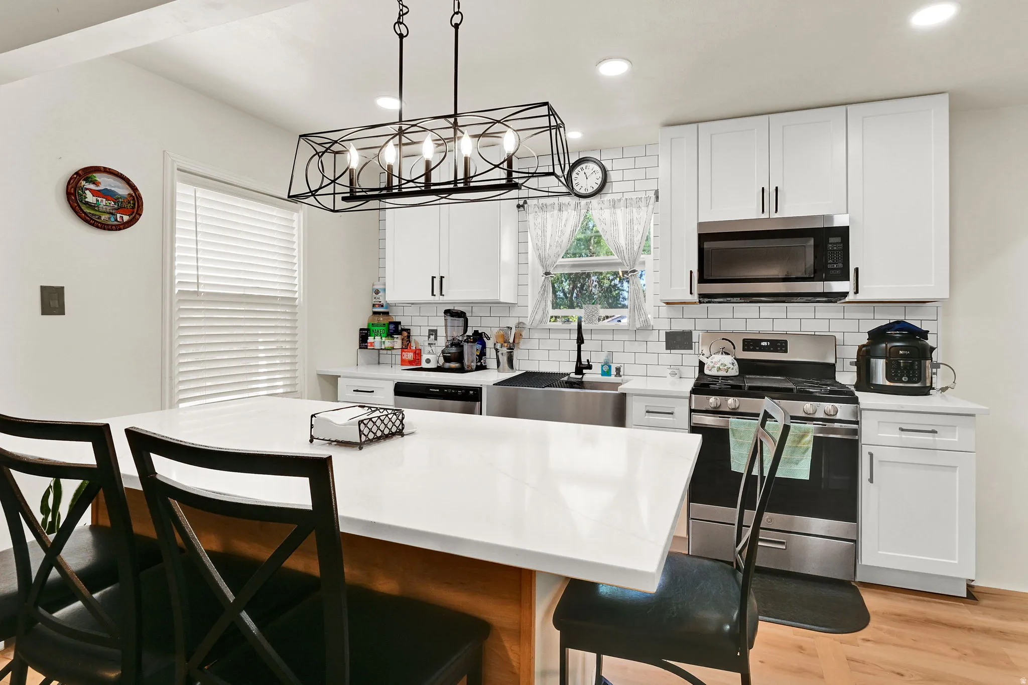 Modern kitchen featuring a large central island with a light-toned countertop, white cabinetry with dark hardware, stainless steel appliances, subway tile backsplash, and wood-finish flooring