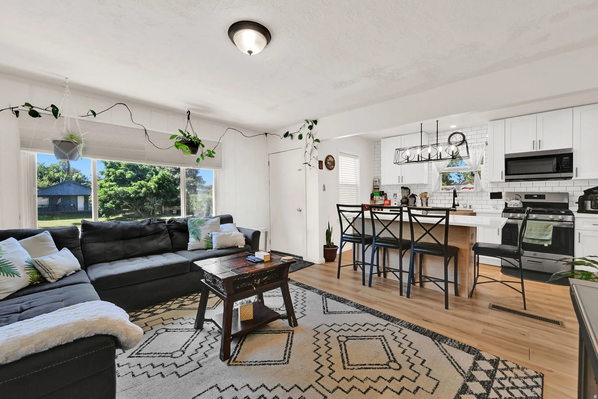 Open-concept living space featuring wood-finish flooring, a kitchen island with seating, white cabinetry, subway tile backsplash, and stainless steel appliances