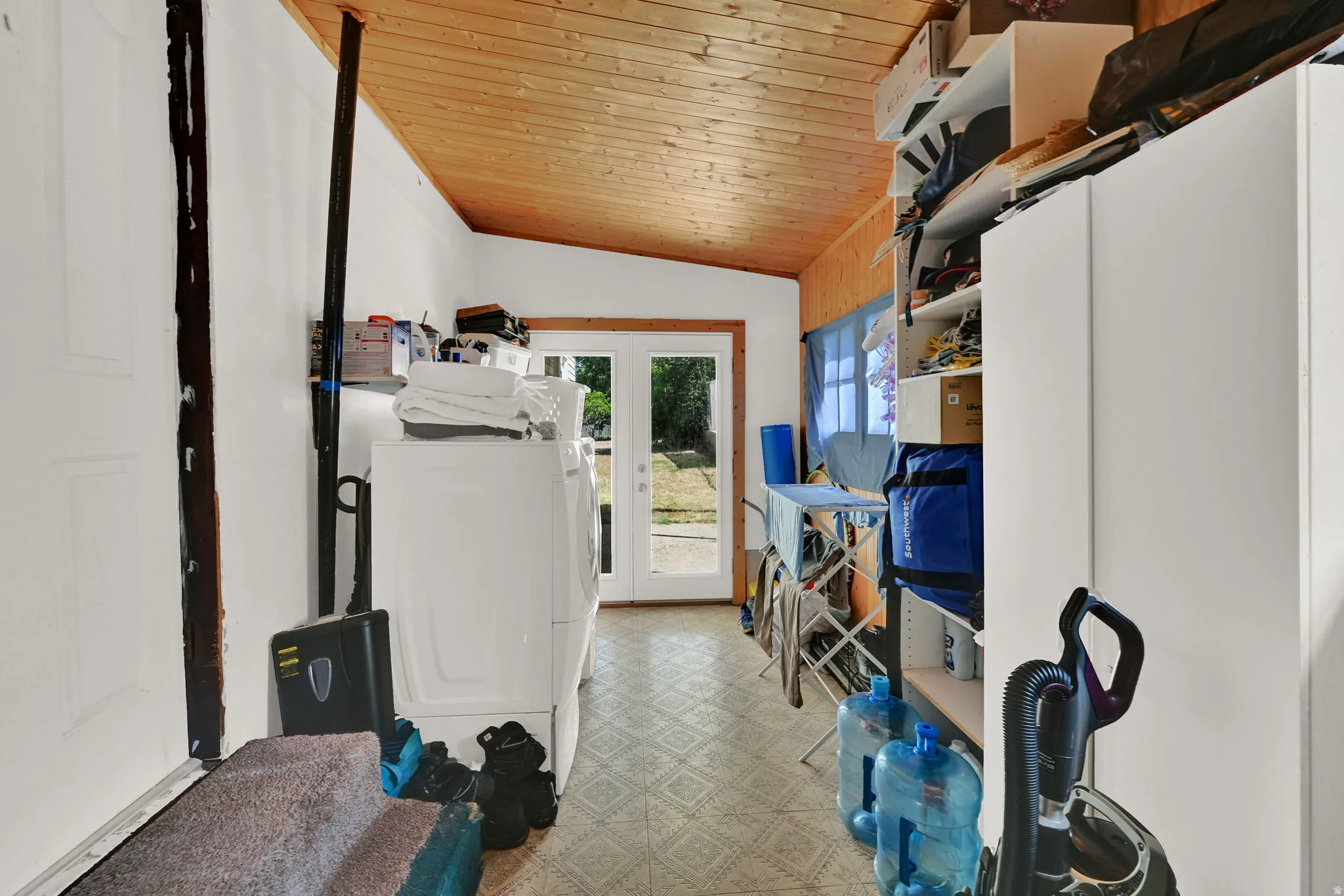 Utility room featuring a sloped wood-finish ceiling, patterned tile flooring, and double glass-paneled doors providing exterior access
