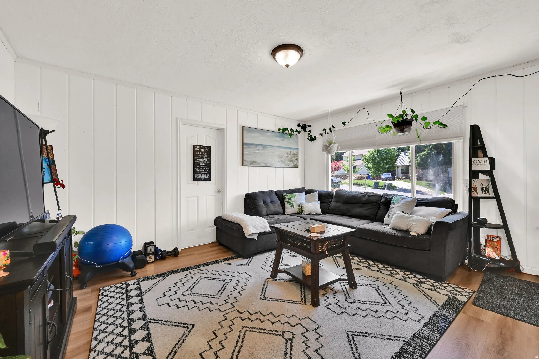 Open-concept living space featuring wood-finish flooring, white vertical wall paneling, and a large window