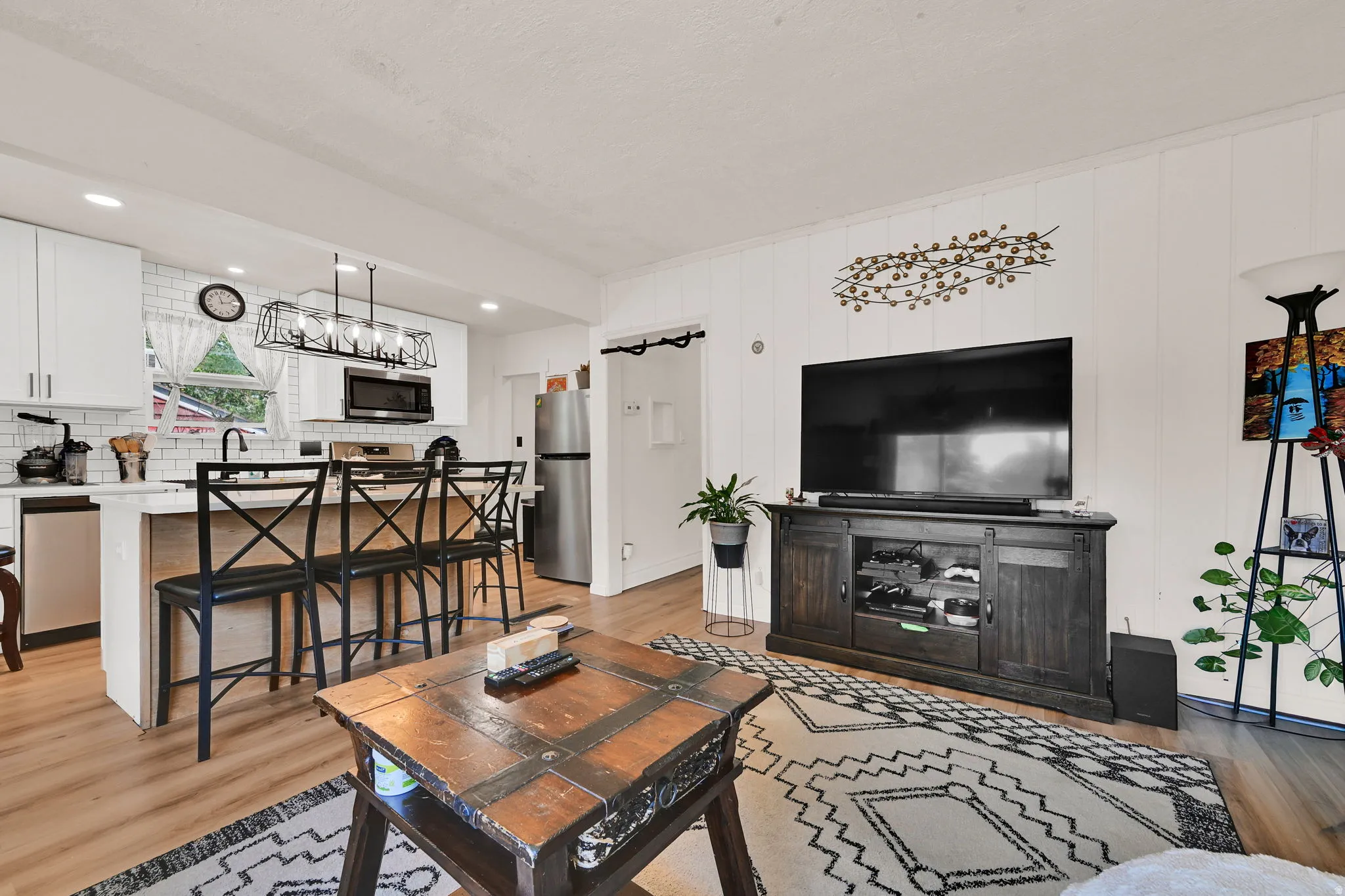 Open-concept living space featuring a kitchen with white cabinetry, subway tile backsplash, and stainless steel appliances