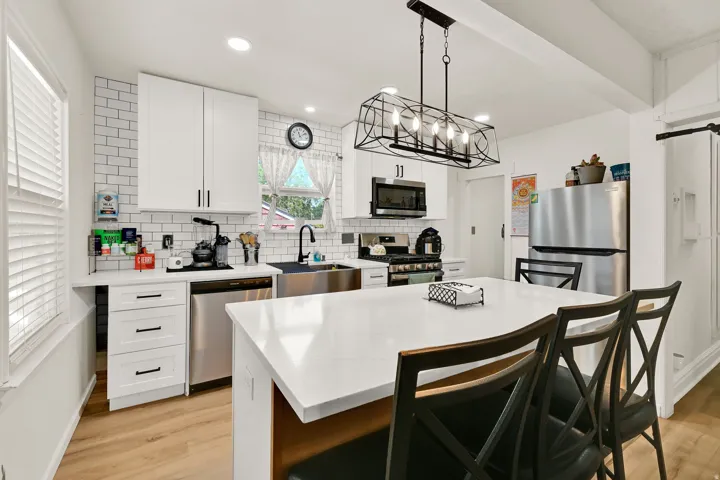 Bright kitchen featuring white cabinetry, subway tile backsplash, stainless steel appliances, a center island with seating, and wood-finish flooring