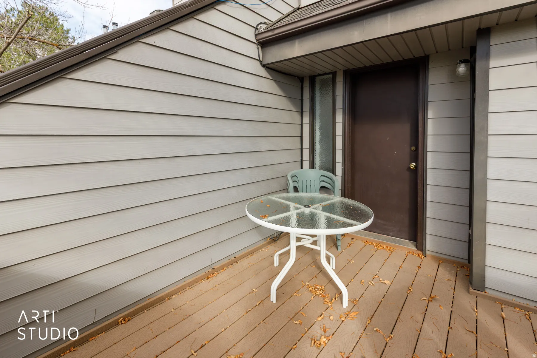 Exterior deck featuring wood-finish flooring, light gray horizontal siding, and a dark brown entry door