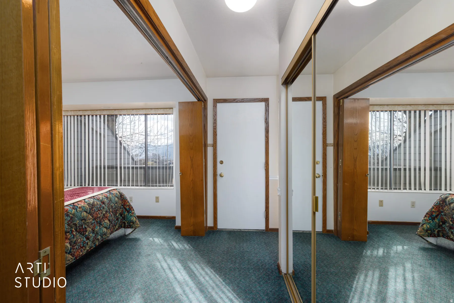 Bedroom featuring a large window with vertical blinds, teal carpet flooring, and a white entry door with a brass-finish knob