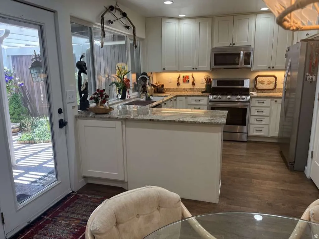U-shaped kitchen featuring wood-finish flooring, white cabinetry, integrated stainless steel appliances, light-toned countertops, and a clear glass door providing access to the exterior