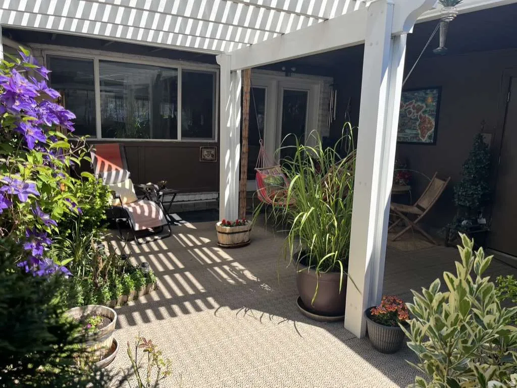 Outdoor patio featuring a white pergola structure over textured flooring, a dual-pane window, and a glass-paned door
