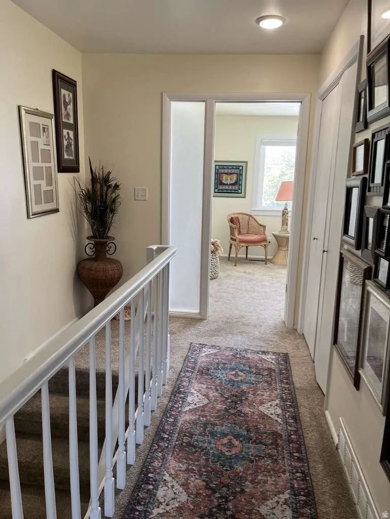 Carpeted hallway with a staircase featuring white wood railings