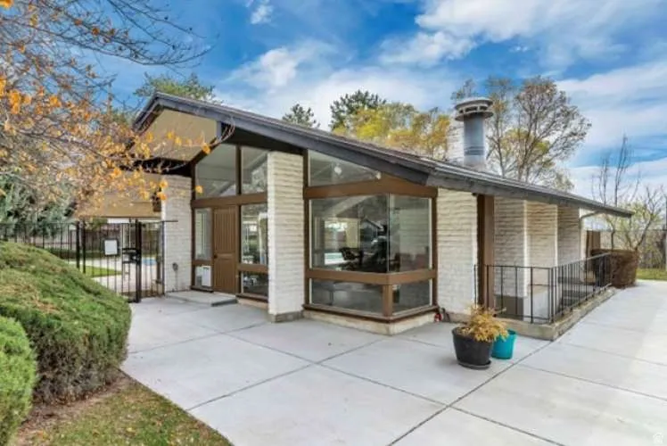 Mid-century modern architecture featuring extensive glass panels, a prominent chimney, and a concrete patio
