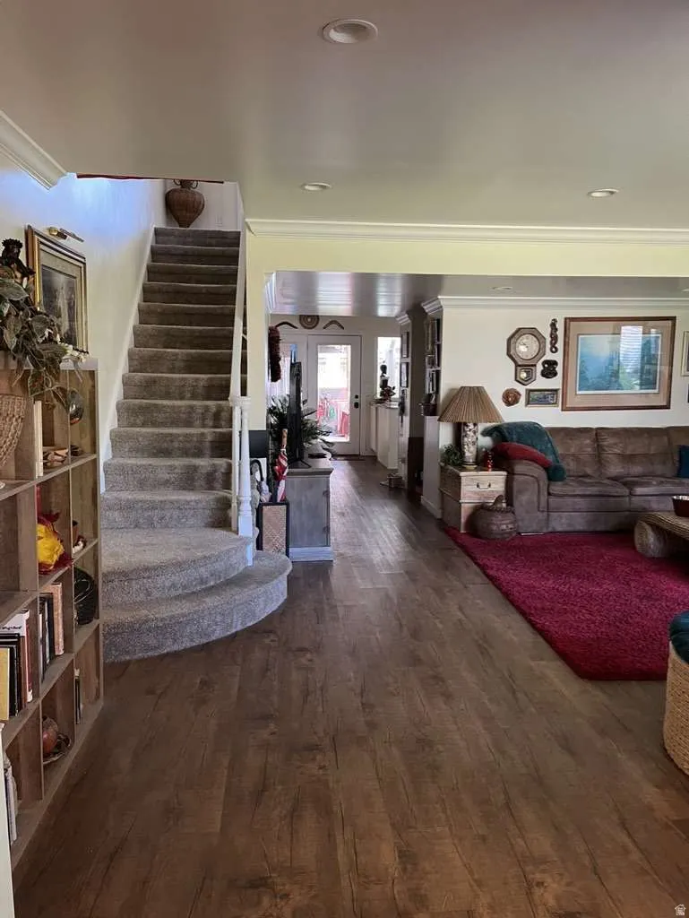Open-concept interior featuring wood-finish flooring, recessed lighting, crown molding, and a carpeted staircase with a rounded base